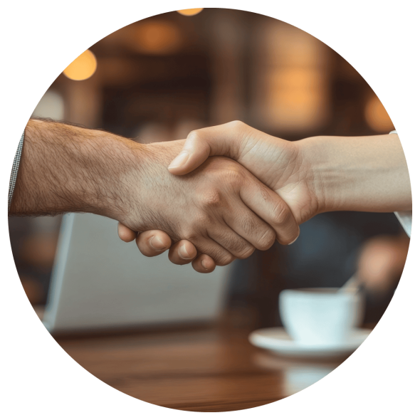 A handshake in a coffee shop, with a laptop and a coffee cup in the background.