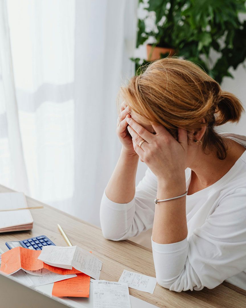 Stressed woman covering her face at desk with receipts and calculator, symbolizing financial stress or budgeting problems.